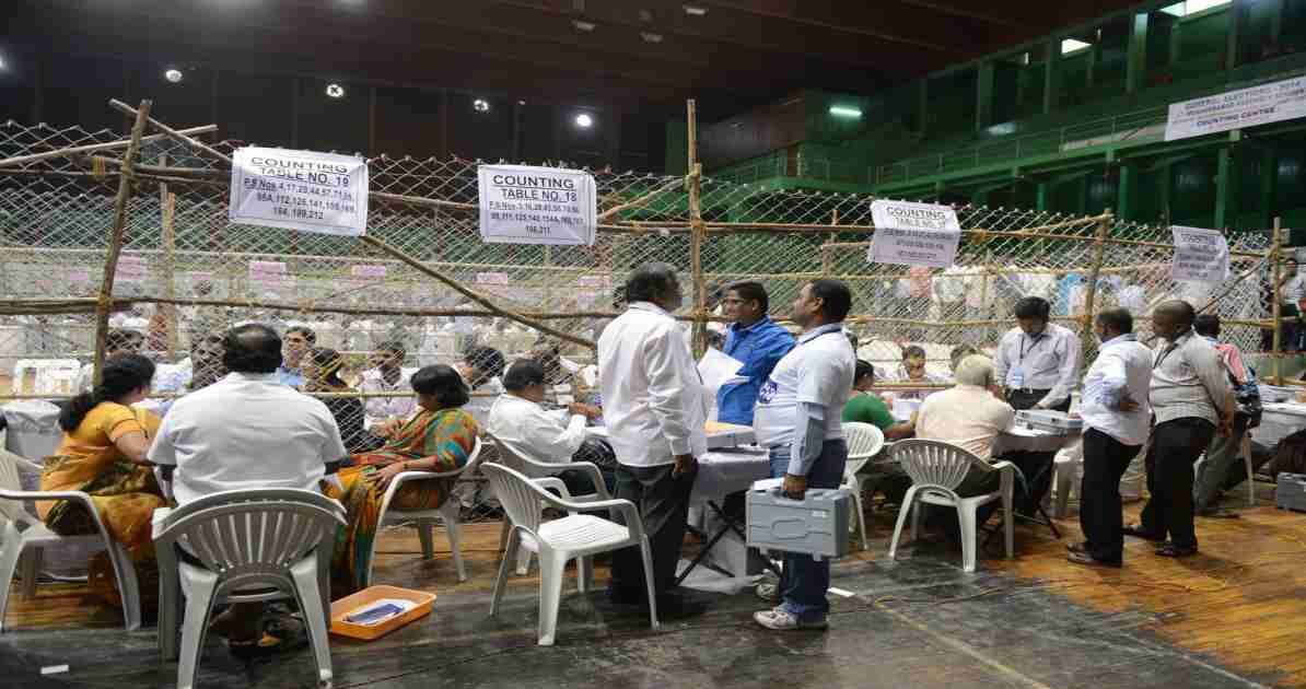 एक टेबल पर रखे मतपत्र और चल रही मतगणना प्रक्रिया, जो चुनाव पारदर्शिता को दर्शाती है