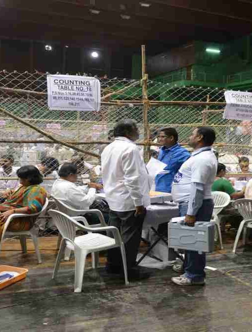 एक टेबल पर रखे मतपत्र और चल रही मतगणना प्रक्रिया, जो चुनाव पारदर्शिता को दर्शाती है