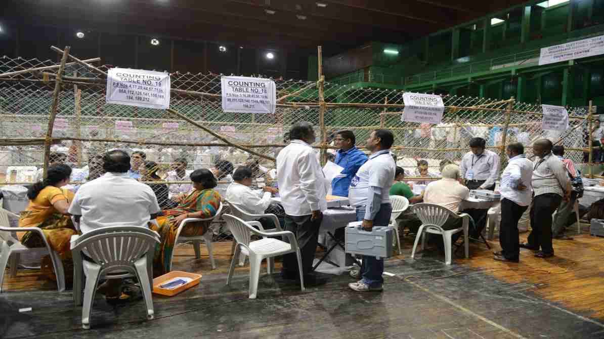 एक टेबल पर रखे मतपत्र और चल रही मतगणना प्रक्रिया, जो चुनाव पारदर्शिता को दर्शाती है