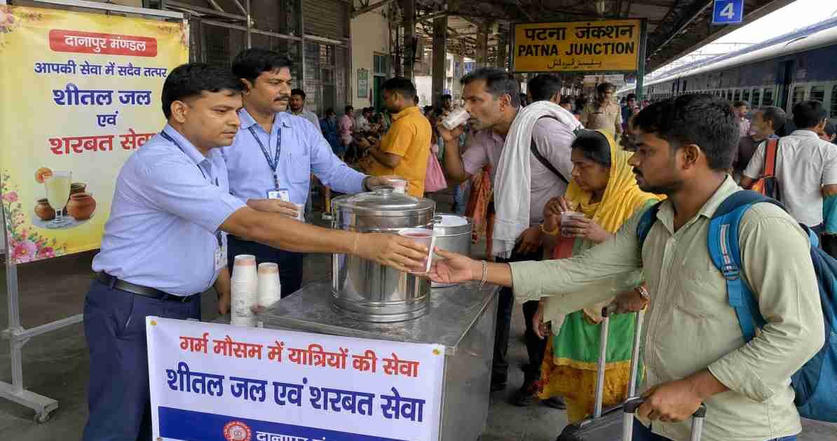 भीषण गर्मी के दौरान पटना जंक्शन प्लेटफॉर्म पर यात्रियों को शरबत और ठंडा पानी बांटते रेलवे कर्मचारी का दृश्य।