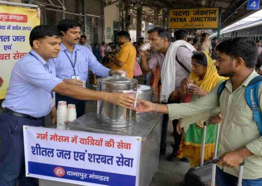 भीषण गर्मी के दौरान पटना जंक्शन प्लेटफॉर्म पर यात्रियों को शरबत और ठंडा पानी बांटते रेलवे कर्मचारी का दृश्य।